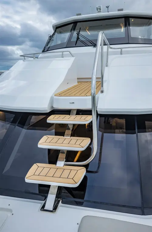 Stainless steel steps with wooden treads leading up to a yacht's upper deck under cloudy skies.